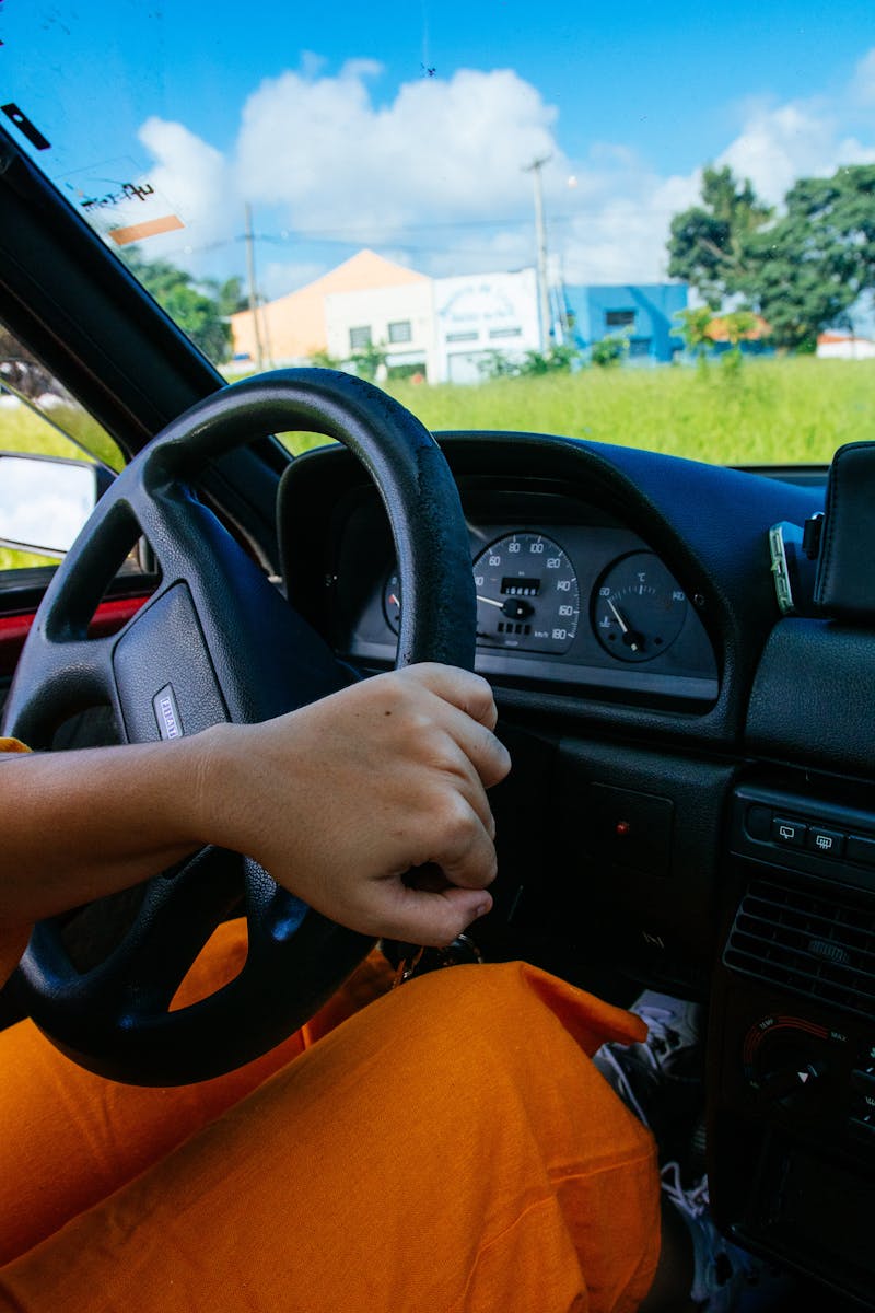 Close-up of a person driving a car, showcasing the steering wheel and dashboard on a sunny day.