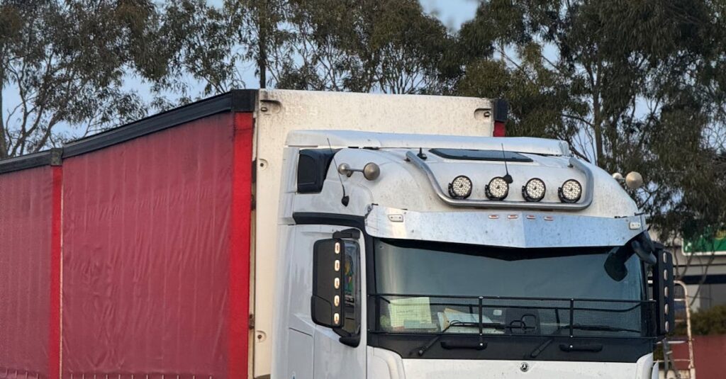 White and red semi truck parked outdoors at logistics hub, ready for transportation.